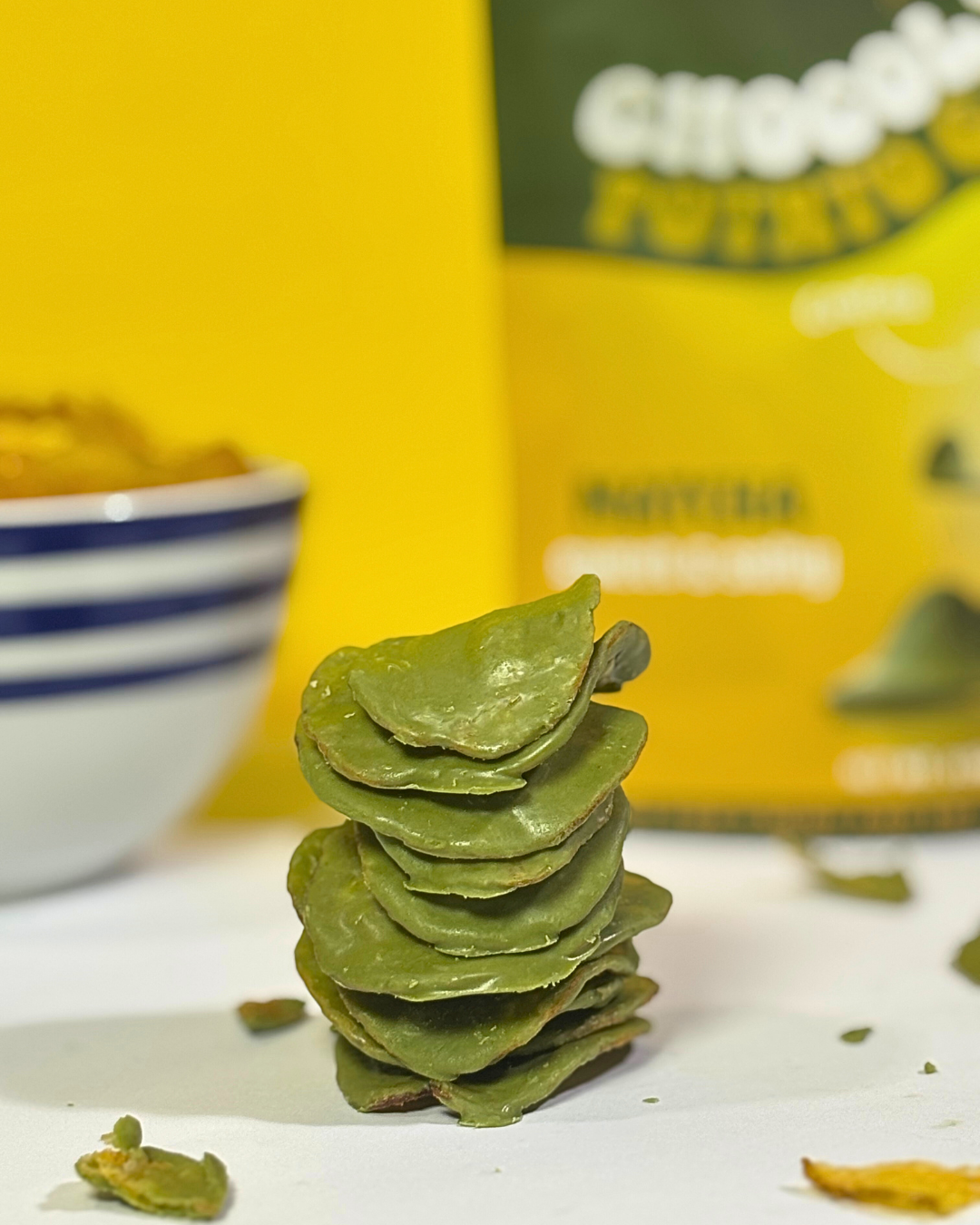 Stack of Matcha Green chocolate-covered potato chip with a bowl of potato chips and matcha packaging on the background